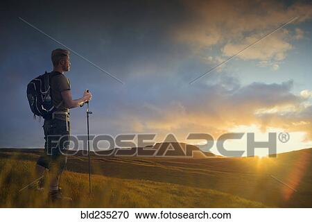 Stock Image - Caucasian hiker admiring landscape at sunset. Fotosearch
