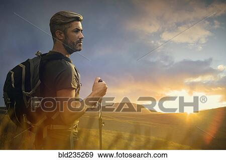 Stock Photo - Caucasian hiker admiring landscape at sunset. Fotosearch