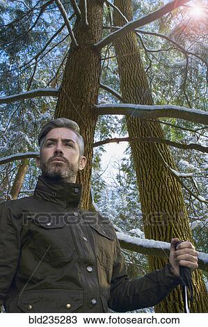 Stock Image - Caucasian hiker holding walking stick under snowy tree. Fotosearch