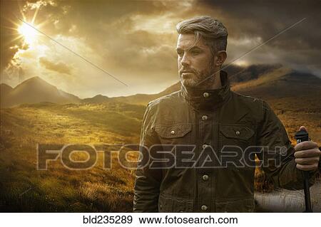Stock Photo - Caucasian hiker holding walking stick near mountain river at sunset. Fotosearch