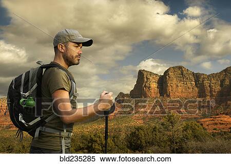 Stock Photography - Caucasian hiker holding walking stick in desert landscape. Fotosearch
