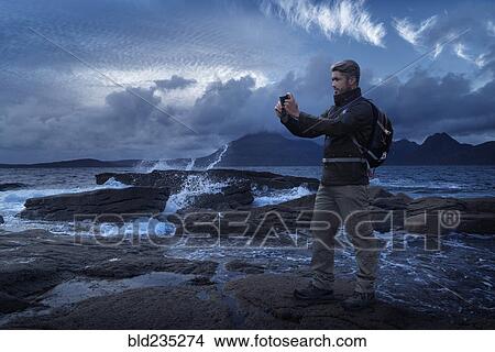 Picture - Caucasian hiker photographing ocean with cell phone. Fotosearch