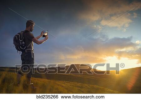 Caucasian hiker photographing sunset with digital tablet View Large Photo Image Stock Photograph - Caucasian hiker photographing sunset with digital tablet. Fotosearch