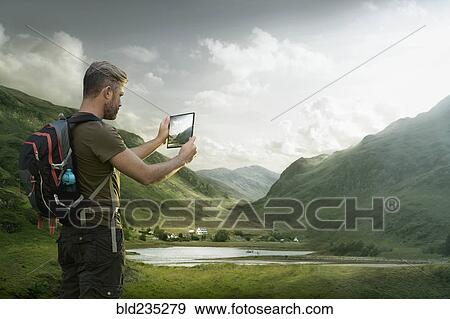 Stock Photo - Caucasian hiker photographing valley lake with digital tablet. Fotosearch