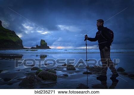 Stock Image - Caucasian hiker standing on beach at sunset. Fotosearch
