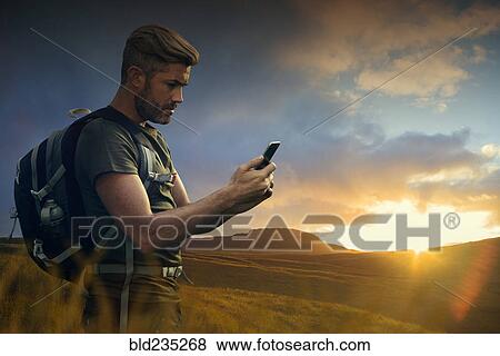 Caucasian hiker texting on cell phone at sunset View Large Photo Image Stock Photo - Caucasian hiker texting on cell phone at sunset. Fotosearch