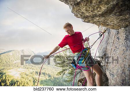 Stock Image - Caucasian man adjusting rope while rock climbing. Fotosearch