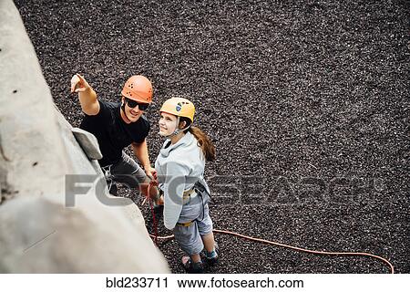 Stock Image - Caucasian man and woman pointing at rock climbing wall. Fotosearch