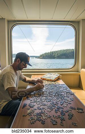 Caucasian man assembling jigsaw puzzle in boat near window View Large Photo Image Picture - Caucasian man assembling jigsaw puzzle in boat near window. Fotosearch