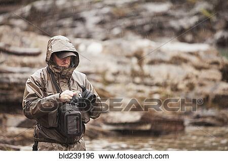 Stock Photograph - Caucasian man at river tying fishing fly. Fotosearch
