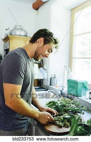 Stock Image - Caucasian man chopping vegetables in kitchen. Fotosearch