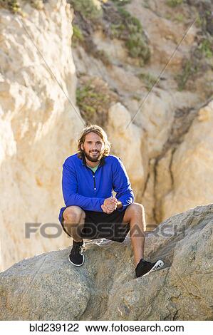 Caucasian man crouching on rock formation View Large Photo Image Stock Image - Caucasian man crouching on rock formation. Fotosearch