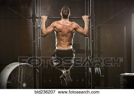 Stock Photo - Caucasian man doing chin-up in gymnasium. Fotosearch