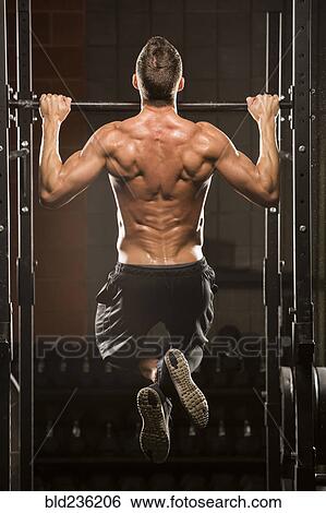 Stock Photograph - Caucasian man doing chin-up in gymnasium. Fotosearch