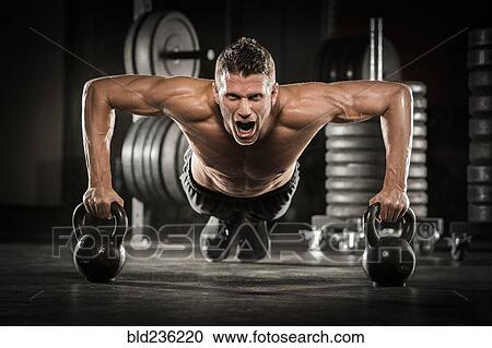 Stock Image - Caucasian man doing push-up using kettlebells in gymnasium. Fotosearch
