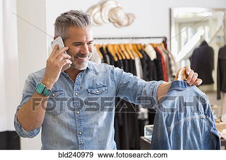 Caucasian man examining shirt talking on cell phone View Large Photo Image Stock Photo - Caucasian man examining shirt talking on cell phone. Fotosearch