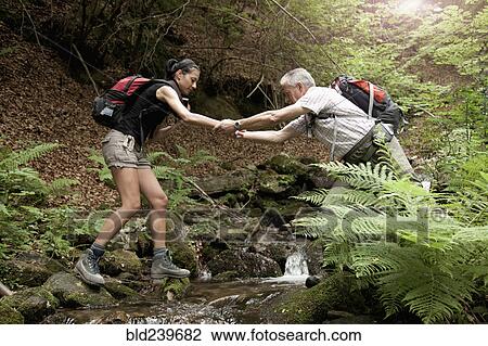 Caucasian man helping woman crossing forest river View Large Photo Image Stock Image - Caucasian man helping woman crossing forest river. Fotosearch