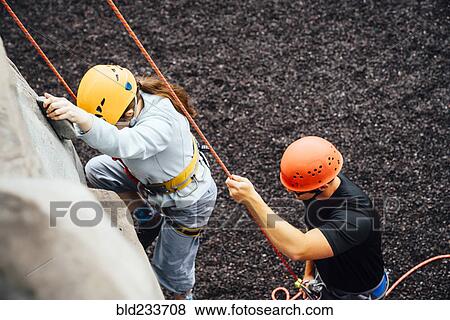 Stock Photo - Caucasian man holding rope for woman climbing rock climbing wall. Fotosearch