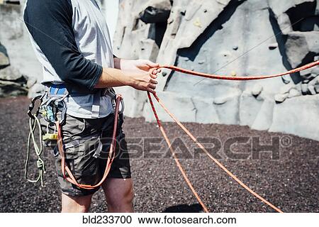 Stock Image - Caucasian man holding ropes at rock climbing wall. Fotosearch