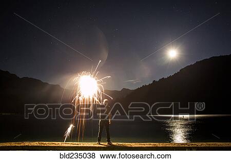 Caucasian man holding sparkler on waterfront at night View Large Photo Image Stock Photo - Caucasian man holding sparkler on waterfront at night. Fotosearch