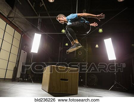Stock Photograph - Caucasian man jumping on box in gymnasium. Fotosearch