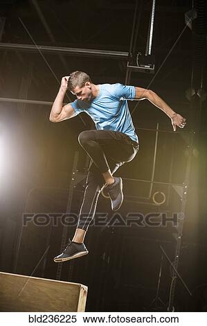 Stock Photography - Caucasian man jumping on box in gymnasium. Fotosearch