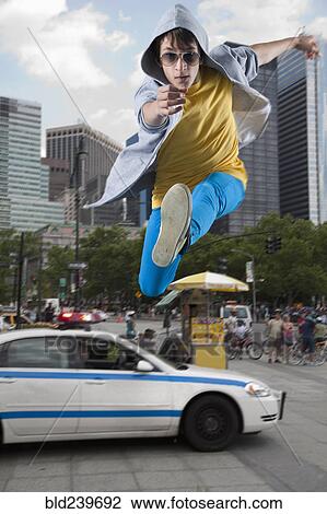 Stock Image - Caucasian man jumping over police car in city. Fotosearch