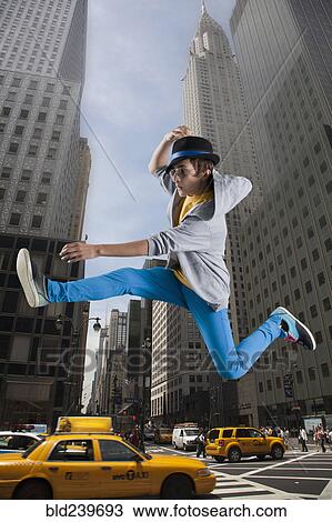 Stock Image - Caucasian man jumping over taxis in city. Fotosearch