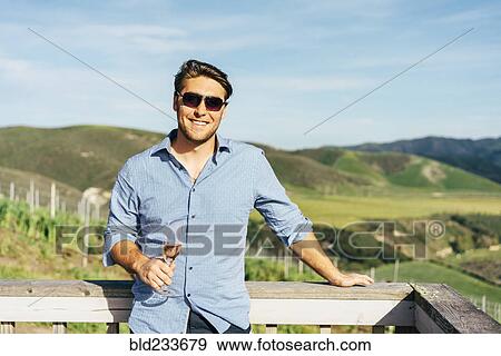 Stock Photo - Caucasian man leaning on balcony drinking wine. Fotosearch