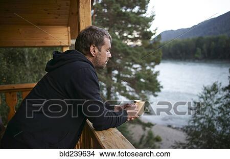 Caucasian man leaning on porch near lake drinking coffee View Large Photo Image Picture - Caucasian man leaning on porch near lake drinking coffee. Fotosearch