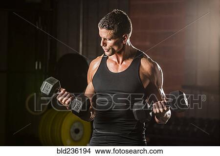 Picture - Caucasian man lifting dumbbells in gymnasium. Fotosearch