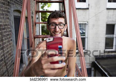 Stock Image - Caucasian man on urban fire escape posing for cell phone selfie. Fotosearch