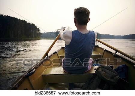 Stock Photo - Caucasian man paddling in rowboat at sunset. Fotosearch