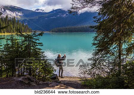 Picture - Caucasian man photographing mountain lake. Fotosearch