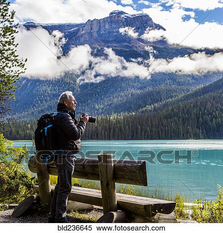 Stock Photography - Caucasian man photographing mountain lake. Fotosearch