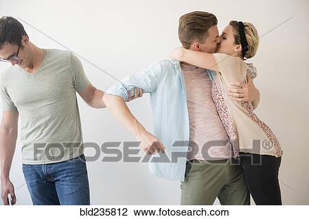 Stock Image - Caucasian man pulling arm of friend kissing girlfriend. Fotosearch