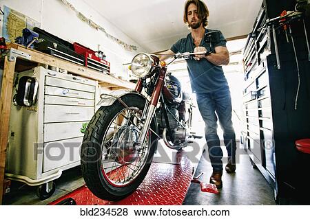 Caucasian man pushing motorcycle on repair stand in garage View Large Photo Image Stock Photo - Caucasian man pushing motorcycle on repair stand in garage. Fotosearch