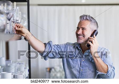 Stock Photo - Caucasian man reaching for glassware talking on telephone. Fotosearch