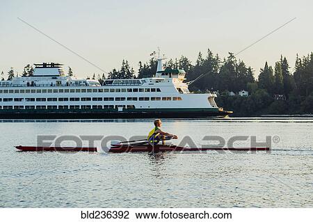 Stock Image - Caucasian man rowing on lake near cruise ship. Fotosearch