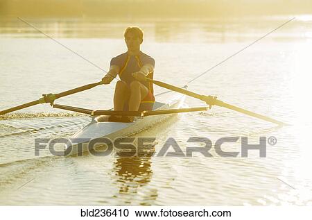 Stock Image - Caucasian man rowing on river at sunset. Fotosearch
