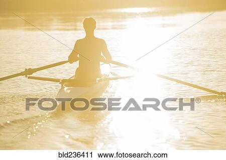 Stock Image - Caucasian man rowing on river at sunset. Fotosearch
