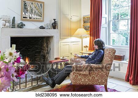 Stock Photography - Caucasian man sitting in armchair near fireplace drinking cocktail. Fotosearch