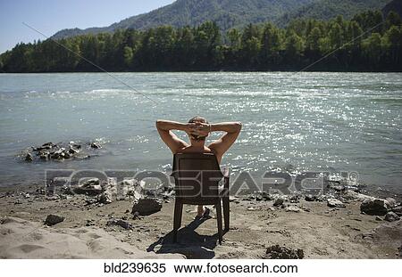 Stock Photography - Caucasian man sitting in chair sunbathing near river. Fotosearch