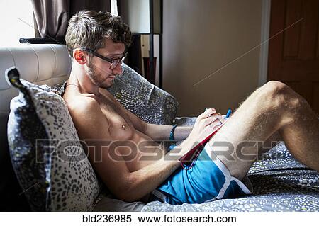Stock Photography - Caucasian man sitting on bed writing in journal. Fotosearch