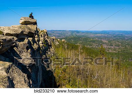 Stock Image - Caucasian man sitting on mountain rock admiring scenic view. Fotosearch