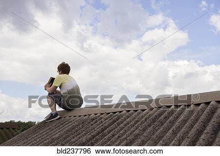 Stock Photograph - Caucasian man sitting on roof holding book. Fotosearch