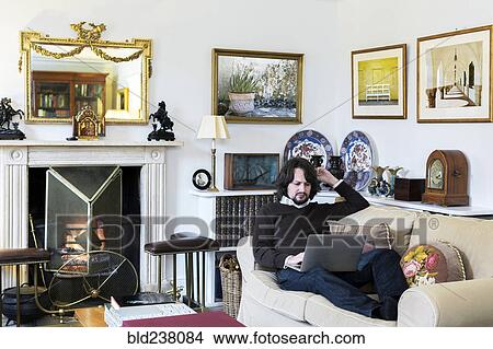 Picture - Caucasian man sitting on sofa using laptop. Fotosearch