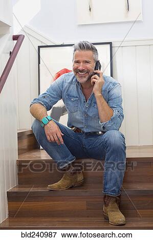Stock Photo - Caucasian man sitting on staircase talking on cell phone. Fotosearch