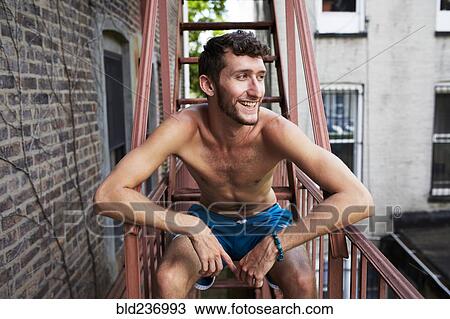 Stock Image - Caucasian man sitting on urban fire escape. Fotosearch