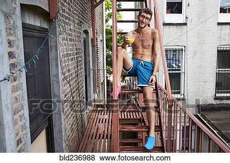 Caucasian man sitting on urban fire escape drinking orange juice View Large Photo Image Stock Photo - Caucasian man sitting on urban fire escape drinking orange juice. Fotosearch
